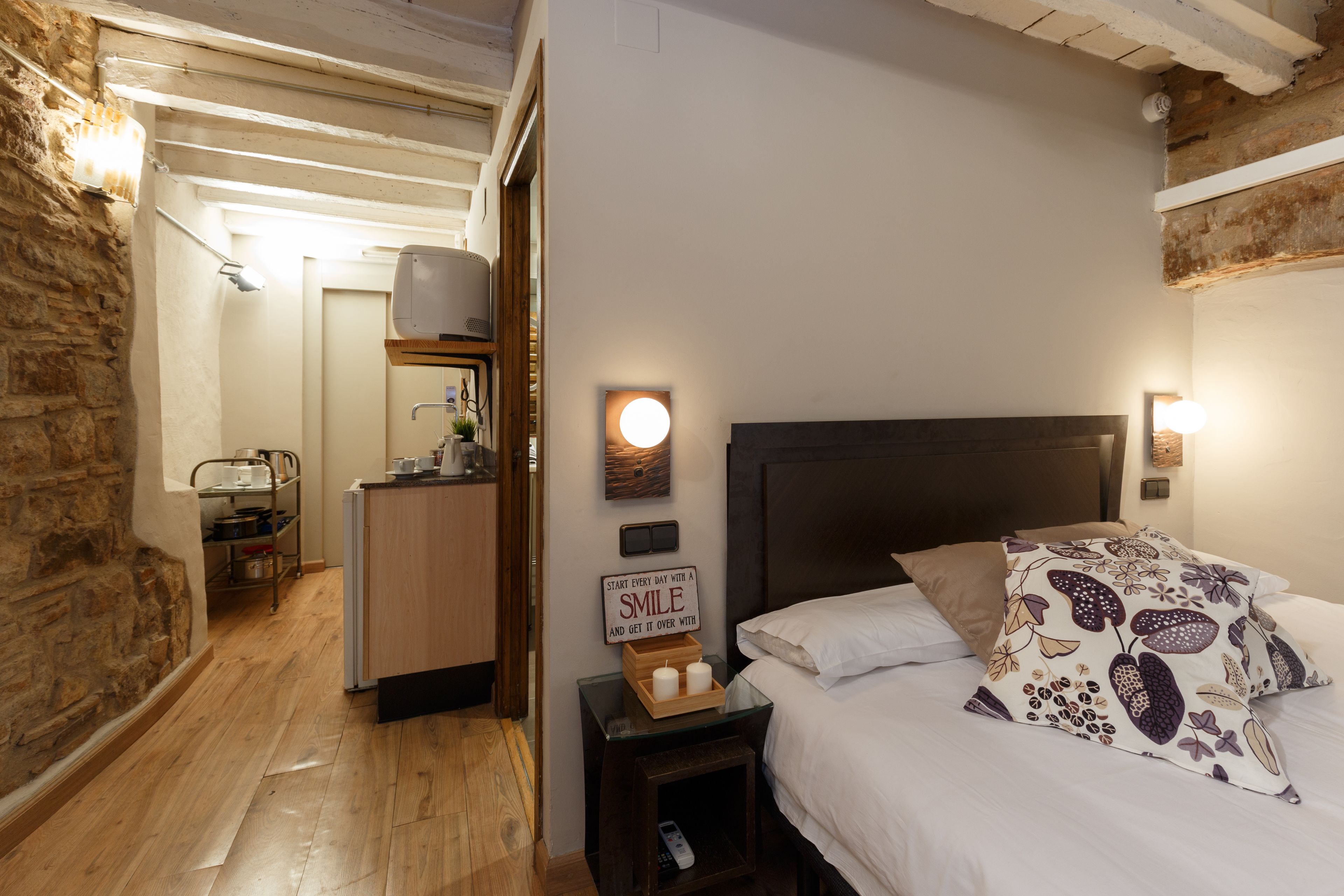 A bedroom with a bed, bedside table, and a sign that says "SMILE AND GET IT OVER WITH".