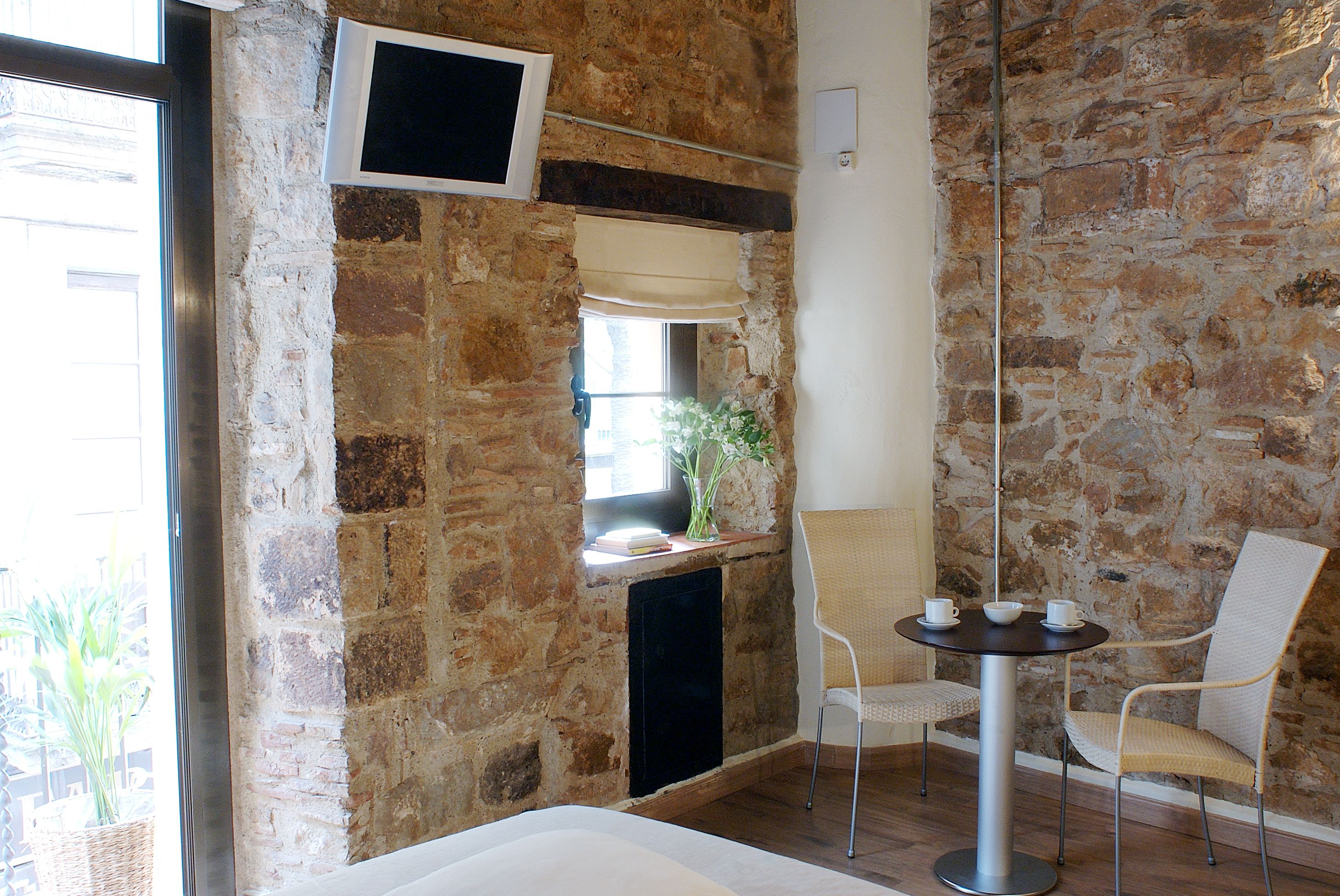Una habitación con pared de piedra, chimenea, televisor montado en la pared y una mesa redonda con sillas.
