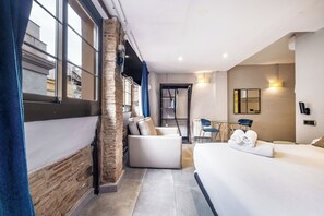A modern hotel room with a large bed, a seating area with a sofa and chairs, a small table, and a view through the window. - AinB Picasso Corders Apartments (Barcelona)
