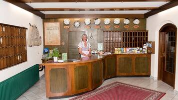 Un área de recepción con un mostrador de madera, una mujer de pie detrás y una pared con relojes y un mapa.
