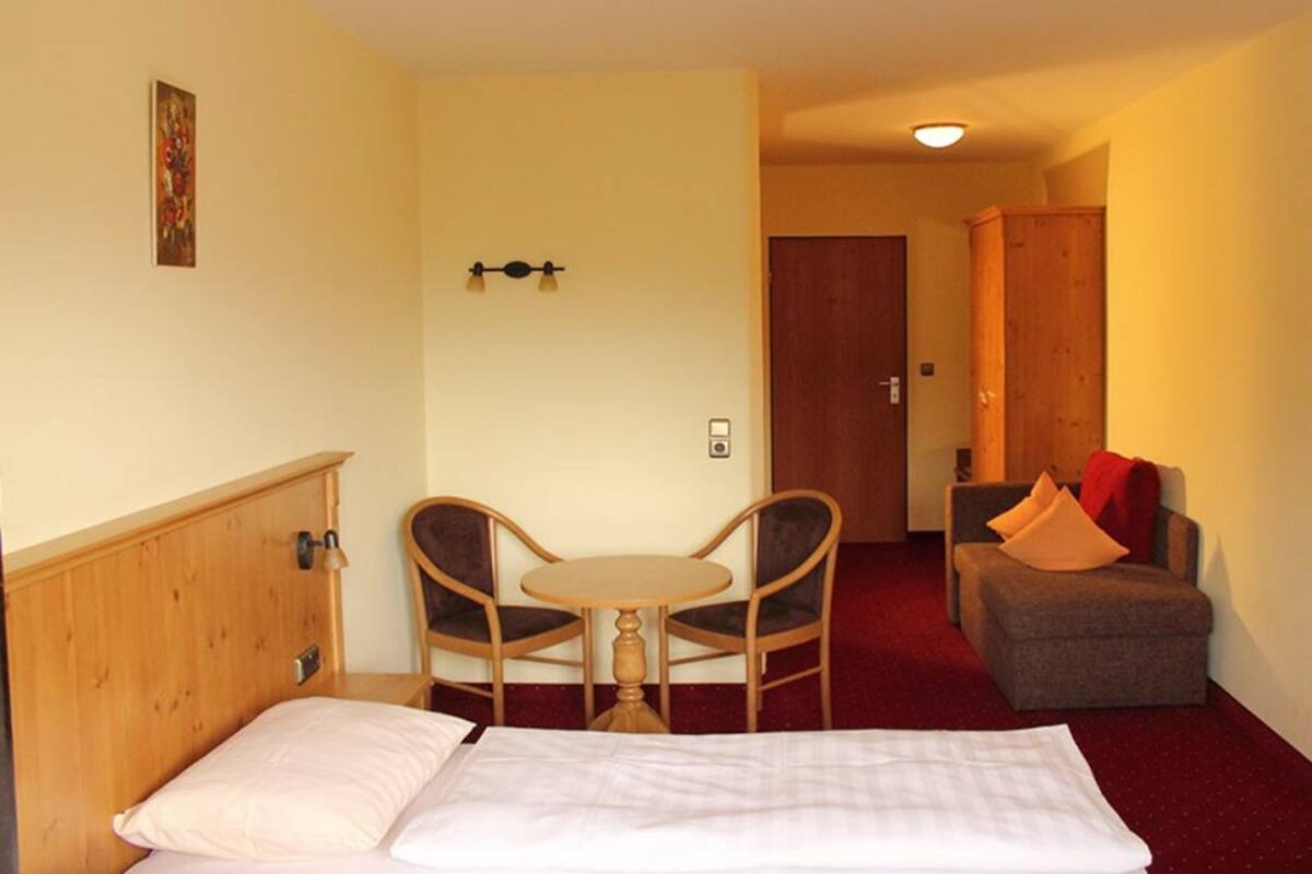 Una habitación de hotel con una cama, una pequeña mesa con dos sillas, un sofá y una puerta al fondo.