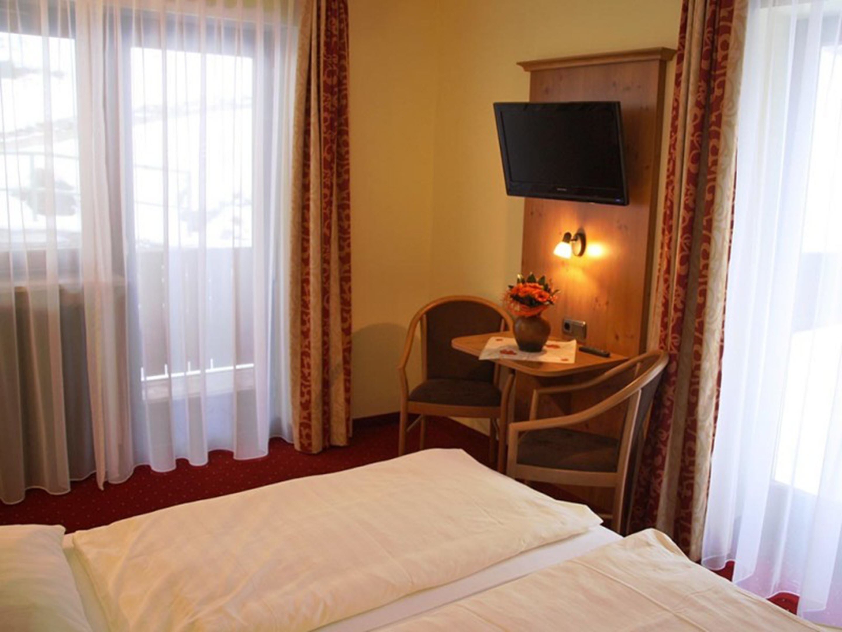 Ein Hotelzimmer mit einem Bett, einem Schreibtisch mit Stuhl, einem Fernseher und einer Vase mit Blumen.