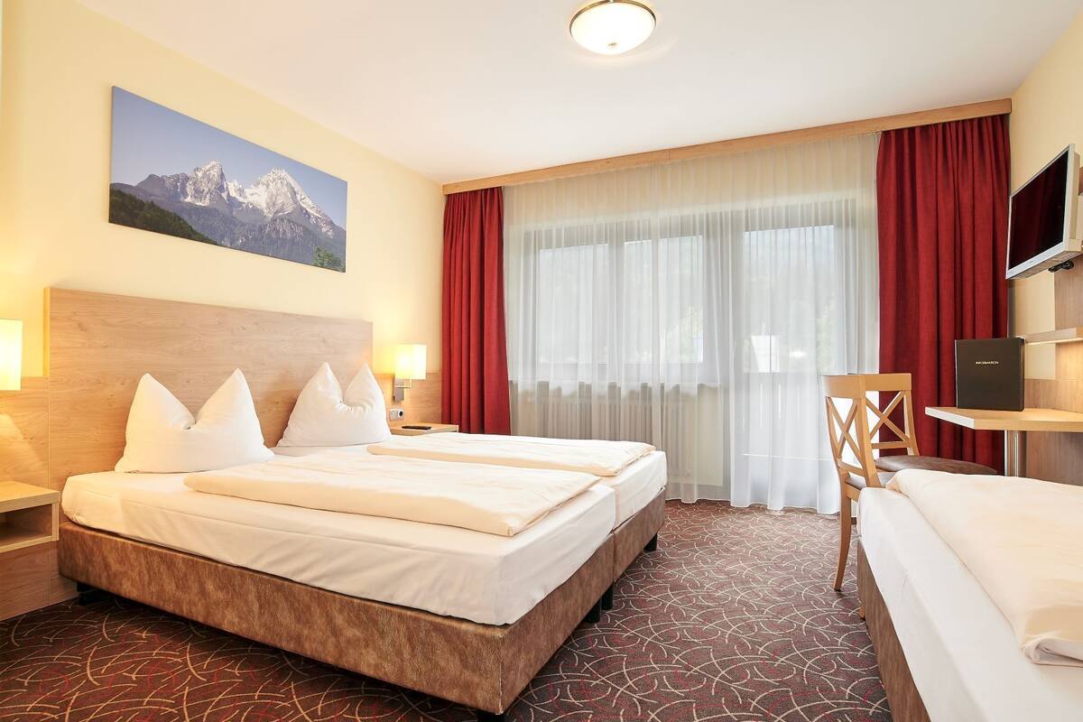 Habitación de hotel con una cama grande, un escritorio, una silla, un televisor y vista a la montaña.