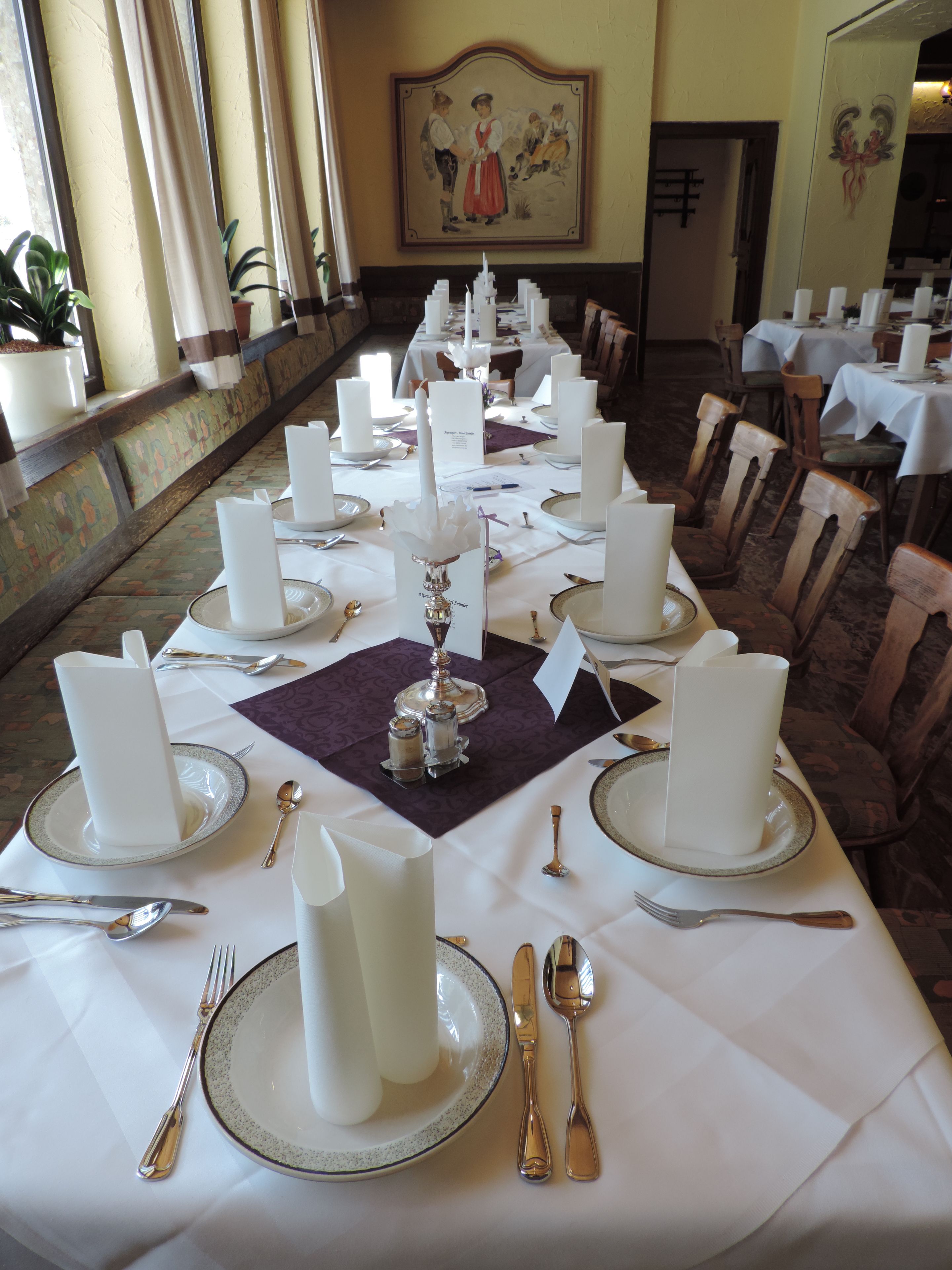 Ein eleganter Speisesaal mit gedeckten Tischen, weißen Tischdecken, Besteck und Kerzen.