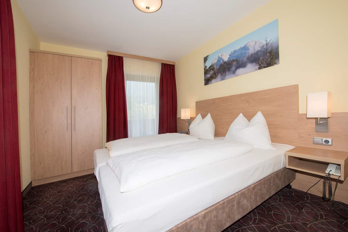 Una habitación de hotel con una cama grande, un armario de madera y un cuadro de un paisaje montañoso.