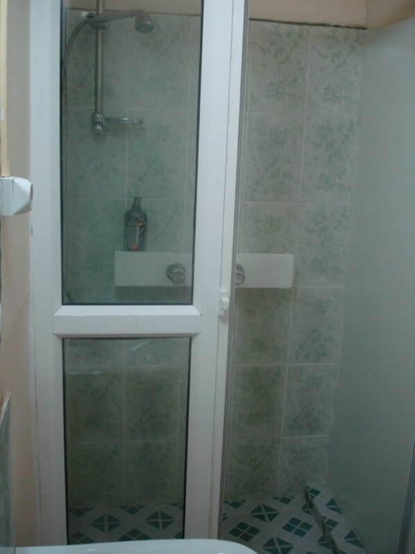 Un baño con ducha envuelta en cristal, paredes de azulejos y suelo con diseño.