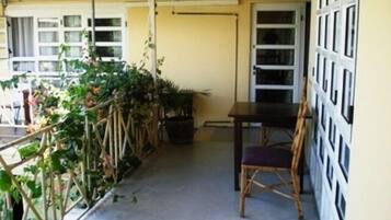 Un balcón con una mesa y una silla, rodeado de plantas en macetas y una baranda blanca.