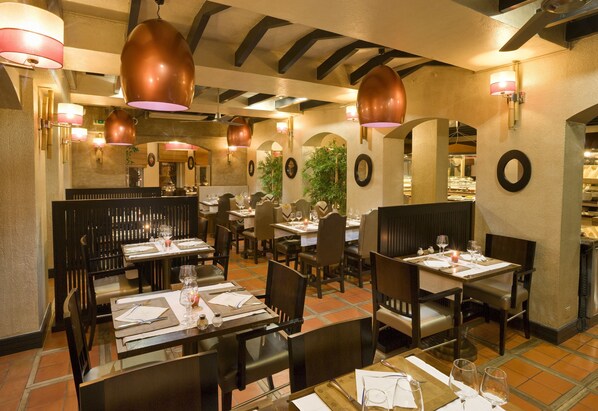 A restaurant with multiple tables and booths, wooden chairs, and hanging copper pendant lights.