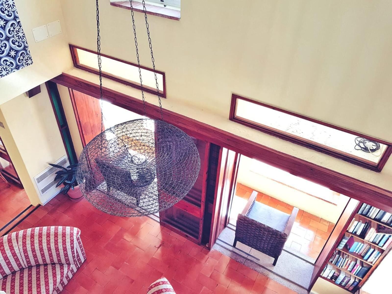 A high-ceiling room with a hanging spherical chandelier, a wooden bench, and a bookshelf.