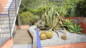 Un jardín con diversas plantas, una terraza de madera y una escalera con barandilla metálica.