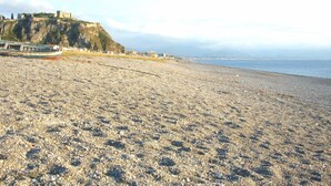 Una playa de guijarros con un castillo en una colina al fondo.