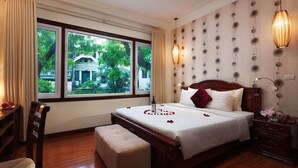 A hotel room with a large bed, a wooden nightstand, a bedside table, and a window with a view of greenery outside. - Hanoi Golden Moon Hotel (Hanoi)