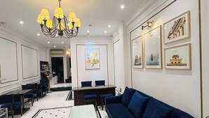 A modern living room with a blue sofa, a white coffee table, and a chandelier. There are framed pictures on the wall and a dining area in the background. - Hanoi Golden Moon Hotel (Hanoi)