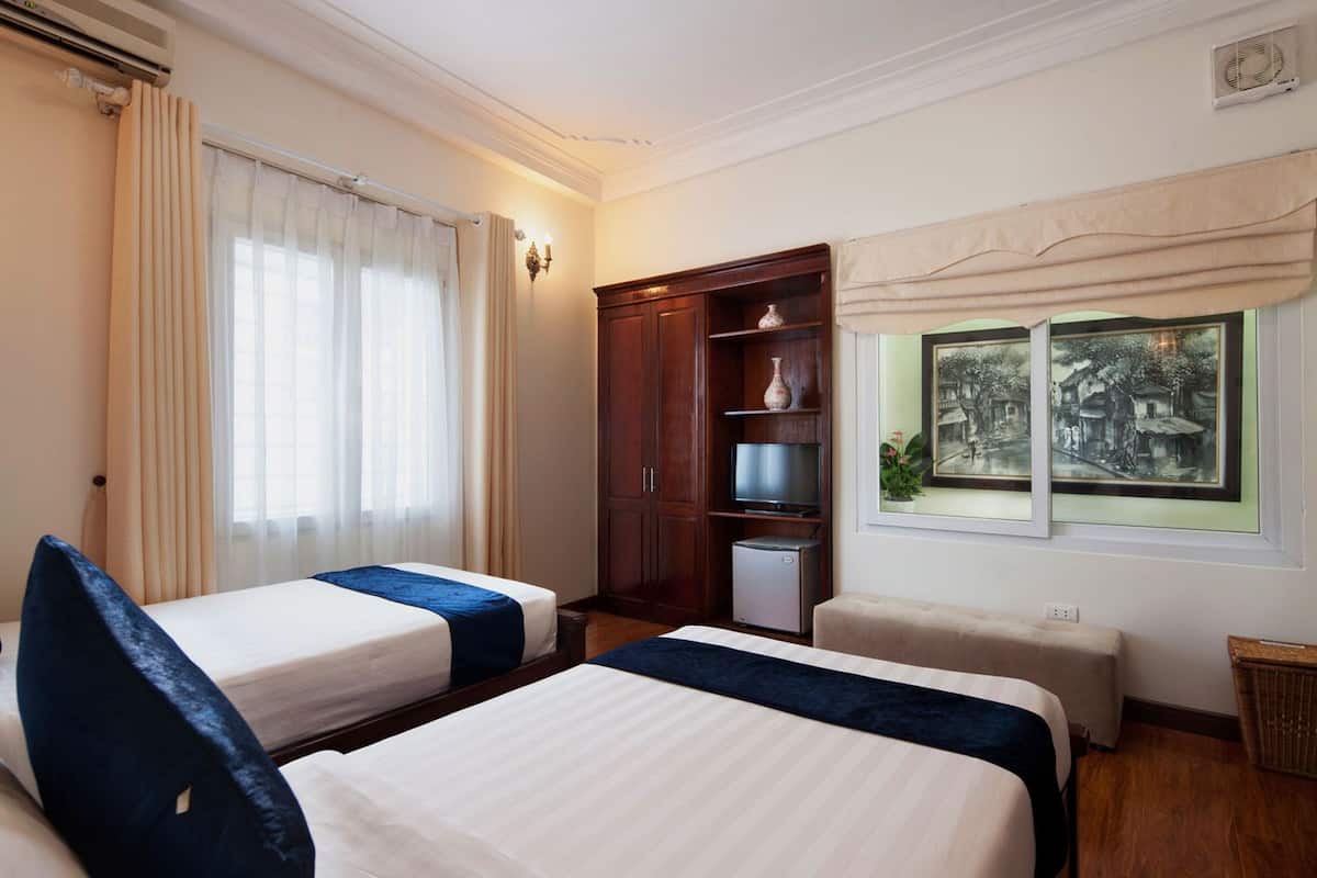 Habitació d'hotel amb dos llits, un armari, una televisió i obra d'art a la paret.
