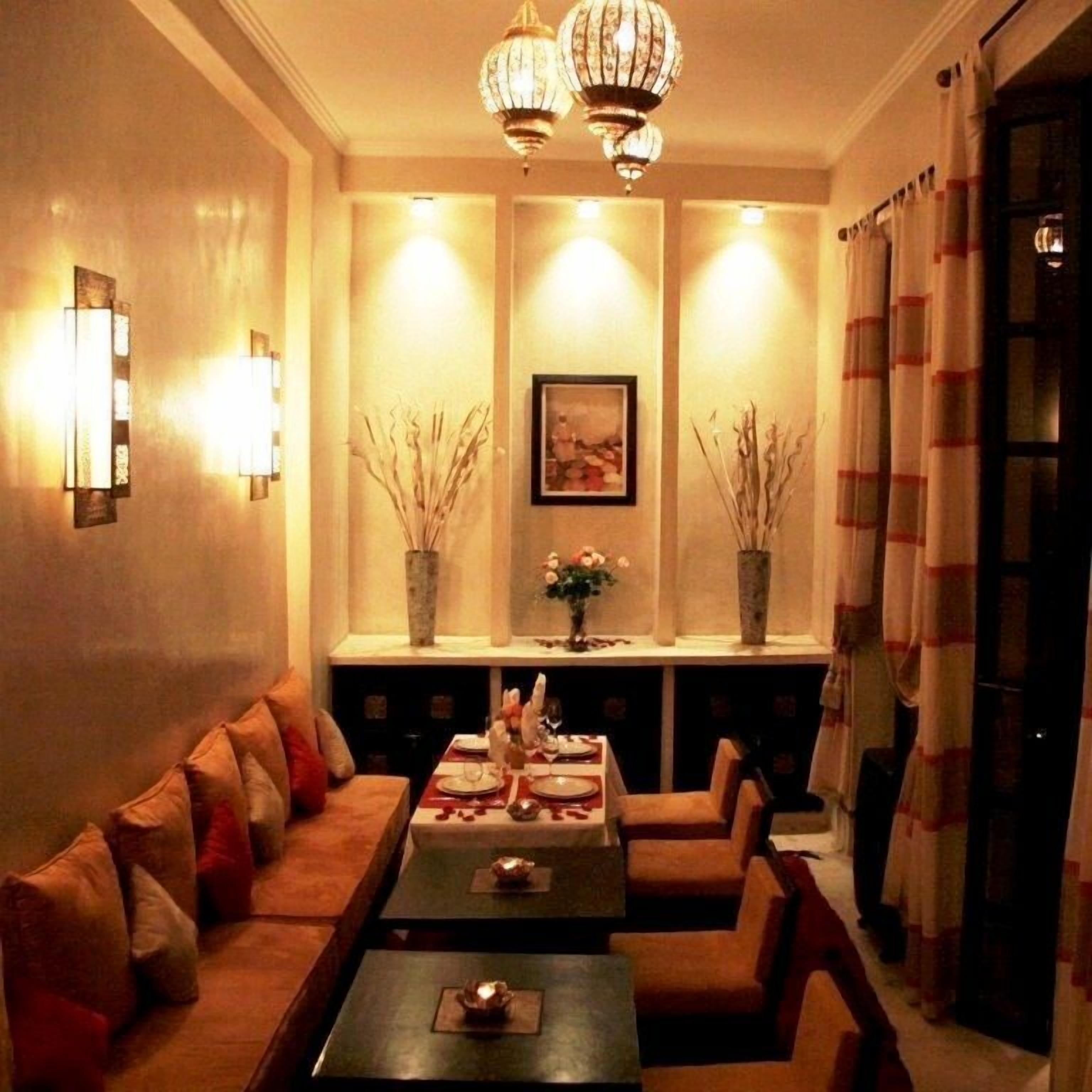 Un salon chaleureux avec un canapé, deux fauteuils, une table basse et une cheminée. On trouve des vases décoratifs sur le manteau de la cheminée, un tableau encadré au-dessus de la cheminée et un lustre au plafond.