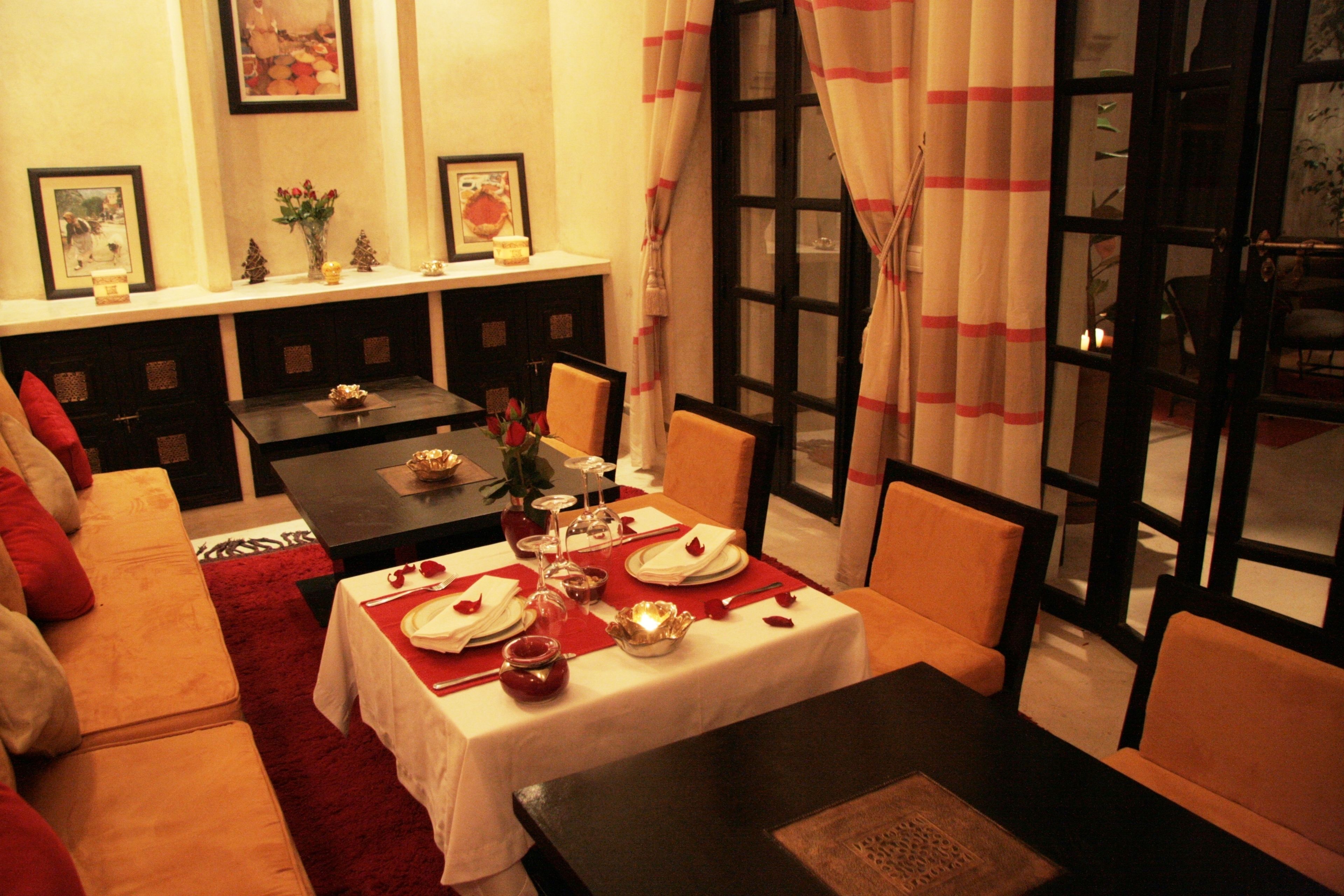 A dining area with a table set for two, a sofa, and a window with curtains.