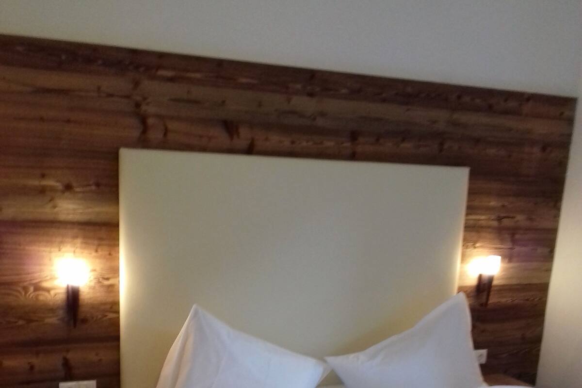 Ein ordentlich bezogenes Bett mit weißen Leinen in einem Zimmer mit Holzwandverkleidung und einem kleinen Nachttisch.