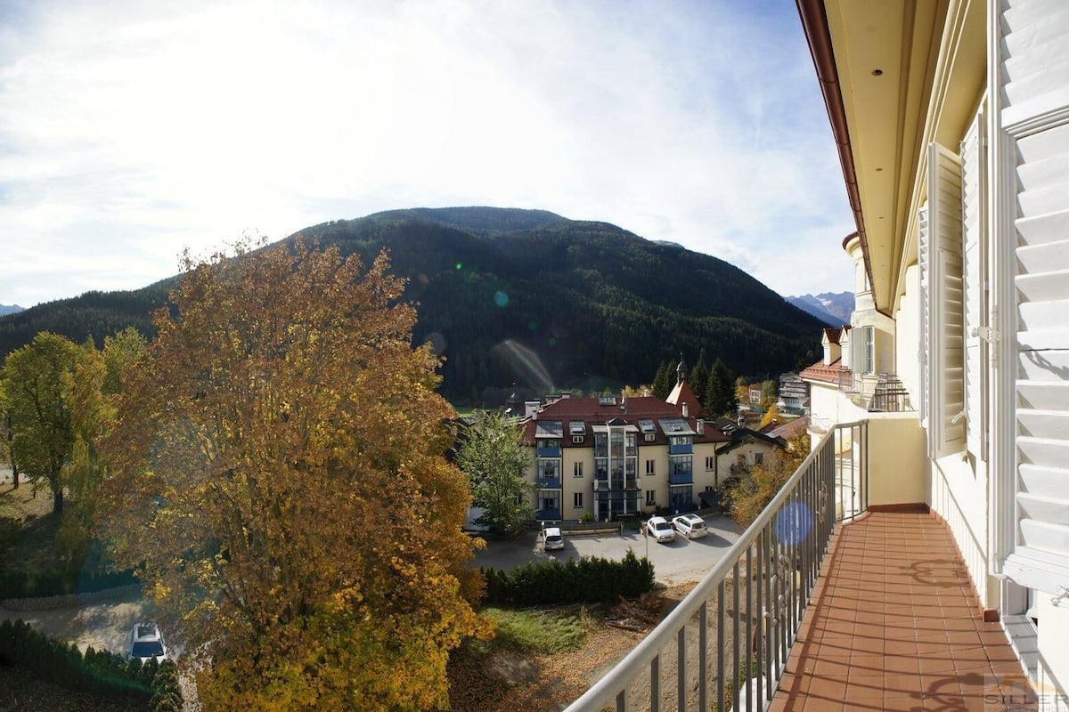 Ein Balkon mit Bergblick, ein Parkplatz und ein Gebäude mit zahlreichen Fenstern.