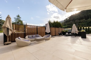 An outdoor patio with wicker furniture, umbrellas, and a view of a forested hillside. - Hotel - Restaurant Schaurhof (Vipiteno)