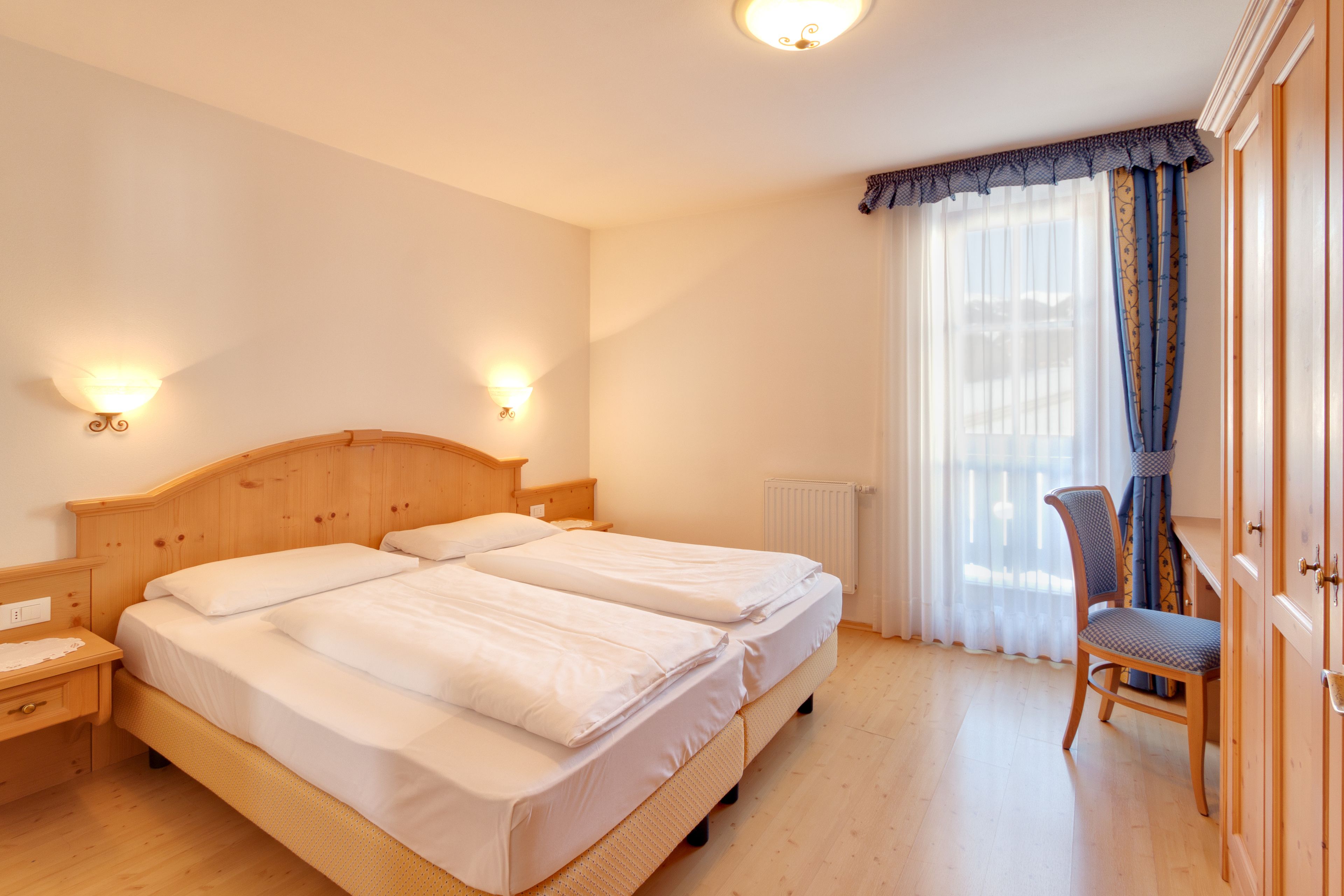 A double bed with a wooden headboard, two bedside tables, a chair, and a window with curtains.