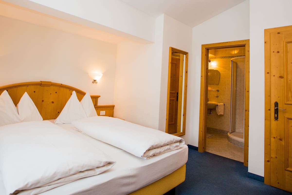 Ein Doppelbett mit weißen Bettbezügen, zwei Wandlampen und Holztüren zu einem Badezimmer.