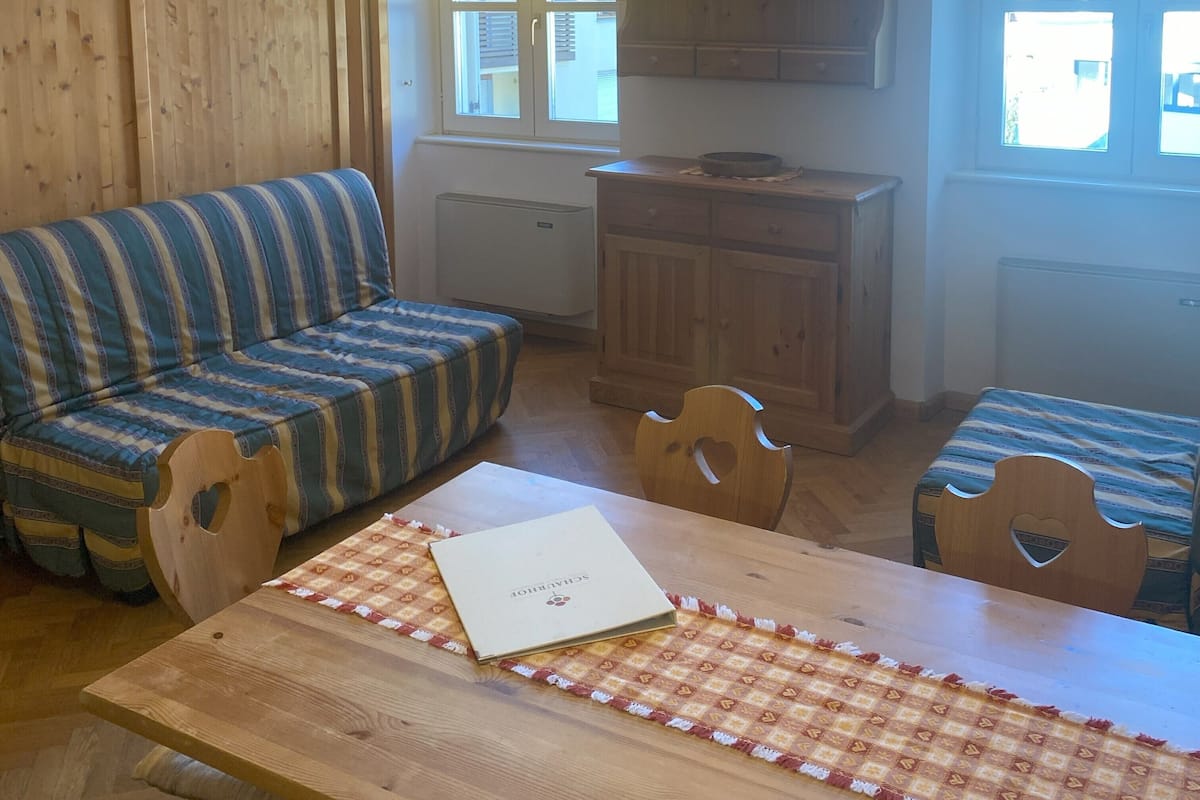 Ein gemütliches Zimmer mit einem gestreiften Sofa, einem Holzesstisch mit kariertem Tischläufer und einer Pendelleuchte.