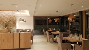 Un espace de salle à manger moderne, avec des meubles en bois, des luminaires suspendus et un mur d’accent en pierre.