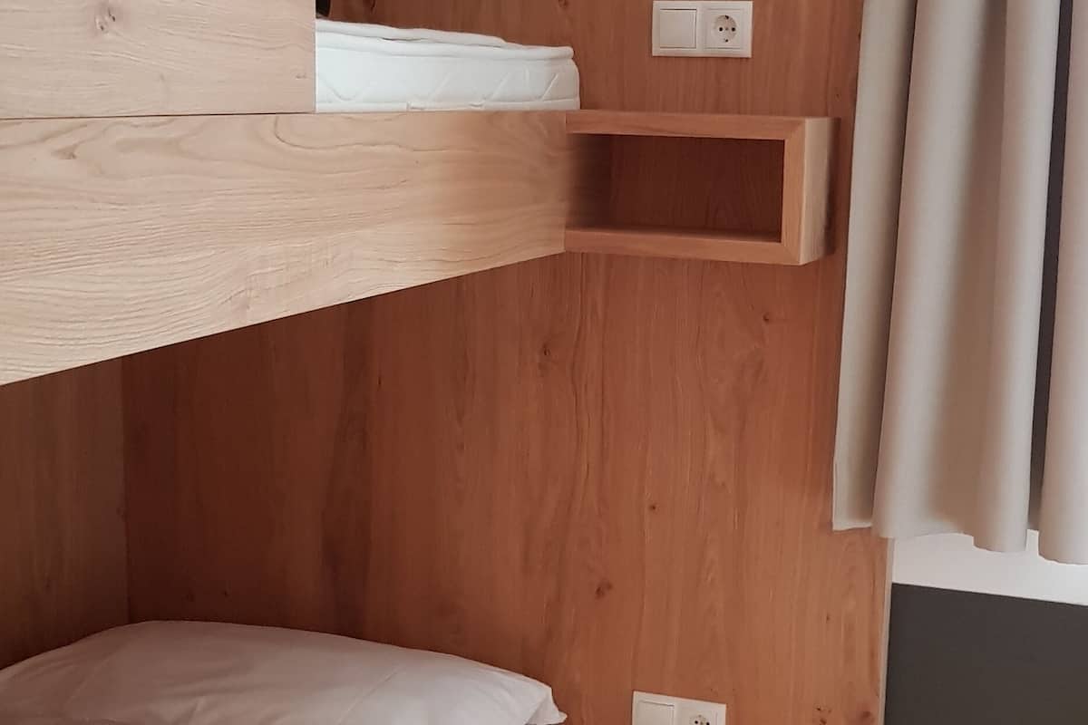 Ein Schlafraum mit Etagenbetten, Holzwänden, einem kleinen Regal und einer Steckdose.