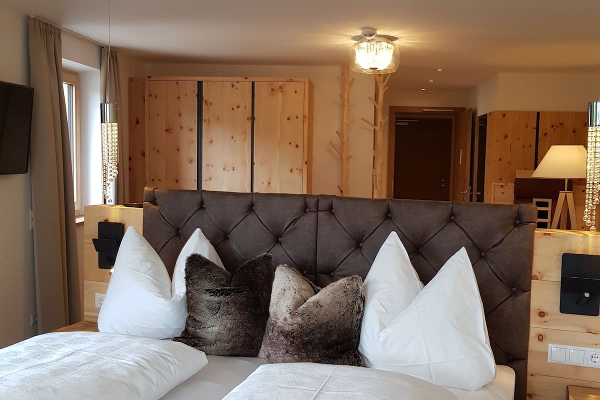 Ein Schlafzimmer mit einer gepolsterten Kopfteile, einem großen Bett mit weißer und brauner Bettwäsche, einem Holzschrank und einem Nachttisch mit einer Lampe.