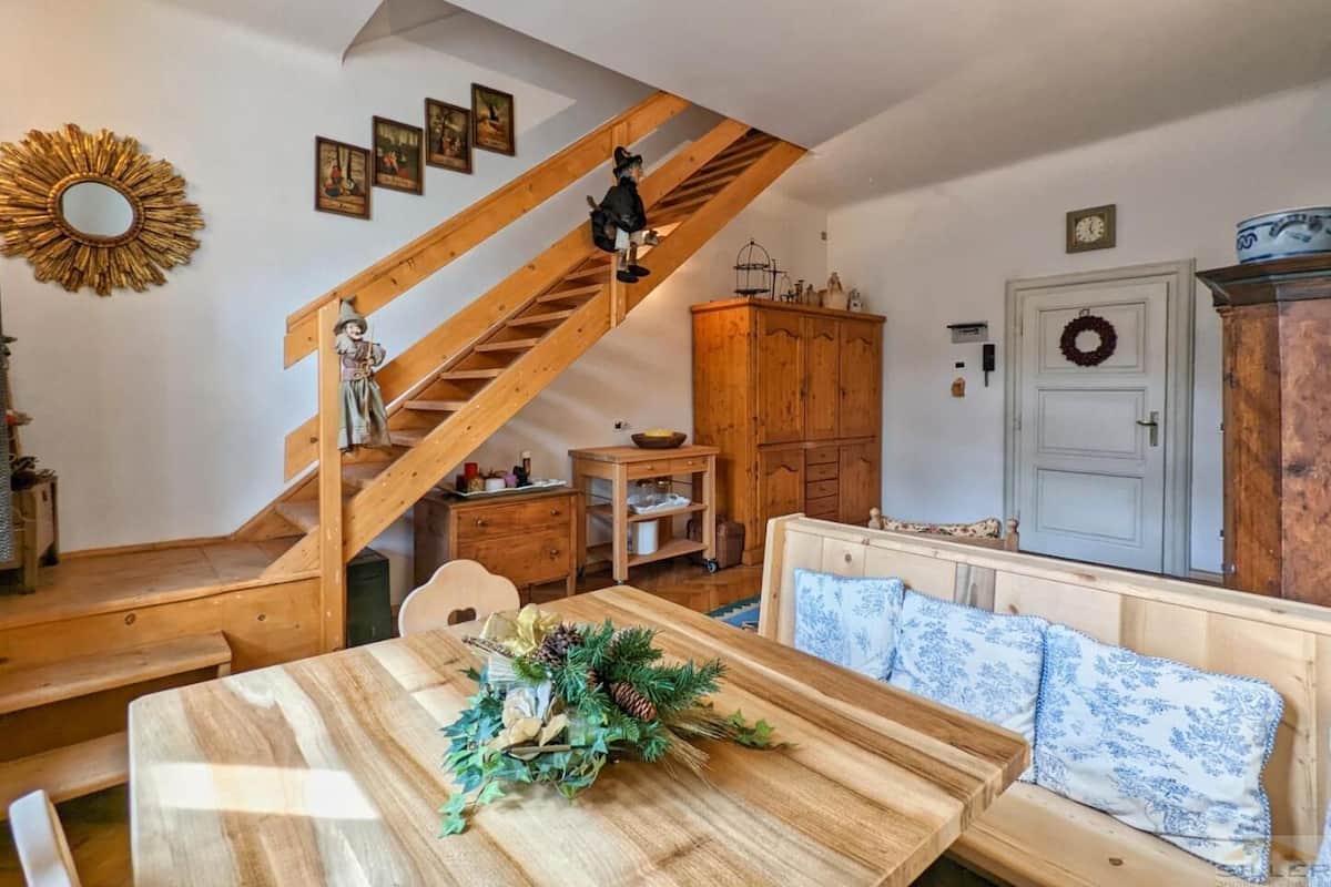 Ein gemütliches Wohnzimmer mit einer Holztreppe, einem Esstisch mit festlichem Mittelstück und einer Couch mit gemusterten Kissen.