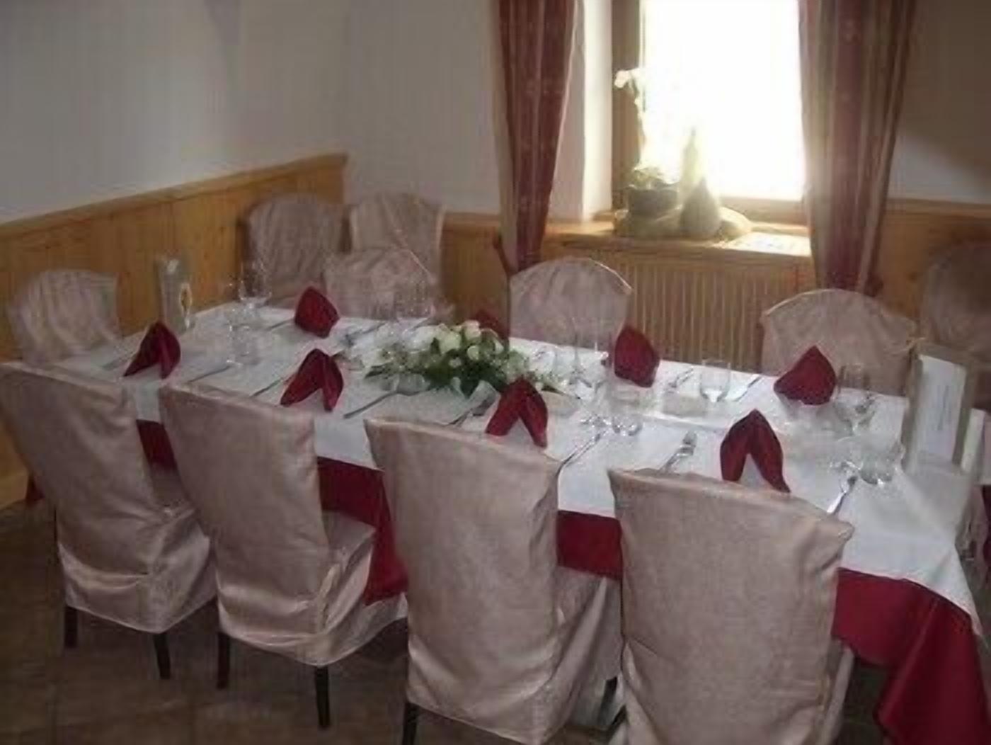 A dining room with a rectangular table set for six, surrounded by six chairs with red sashes.