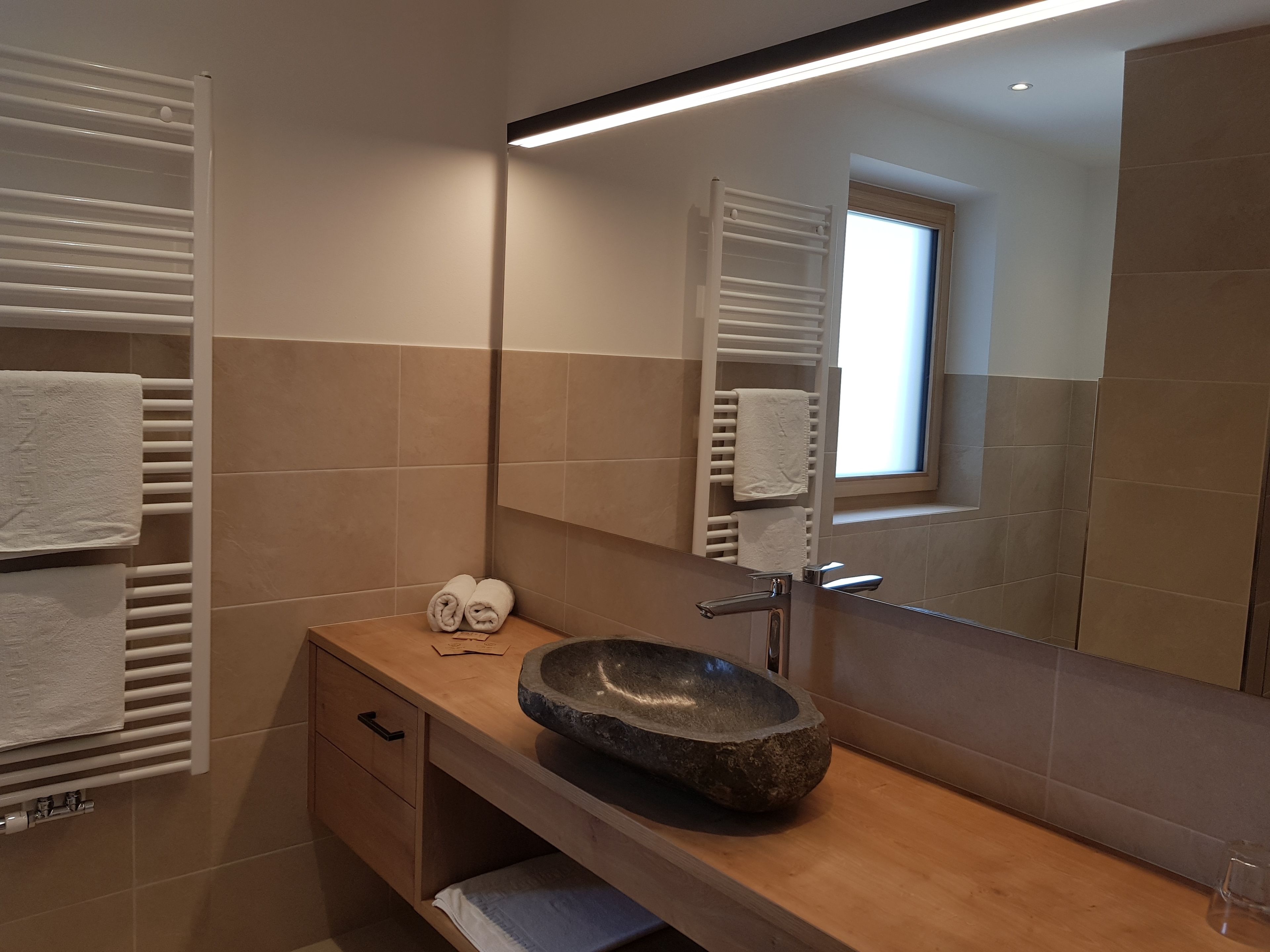 A modern bathroom with a stone sink, white towel racks, and a large mirror.