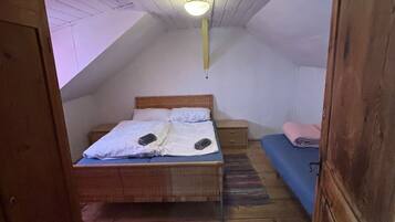 Un dormitorio ático pequeño y de una sola habitación, con techo inclinado, cama de madera, mesita de noche y sofá azul.