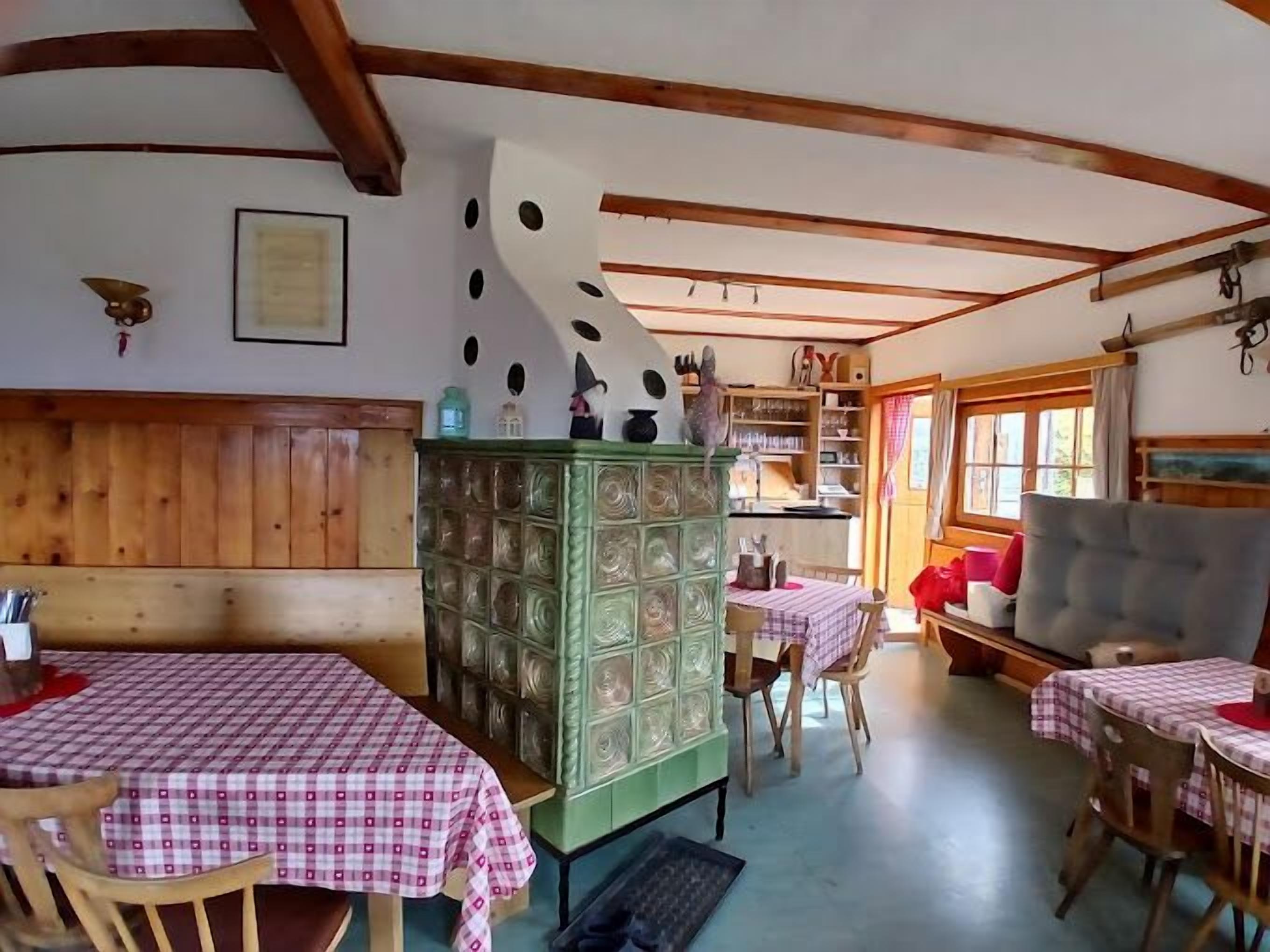 Un rincón comedor acogedor con mesas y sillas de madera, un armario verde y una cocina al fondo.