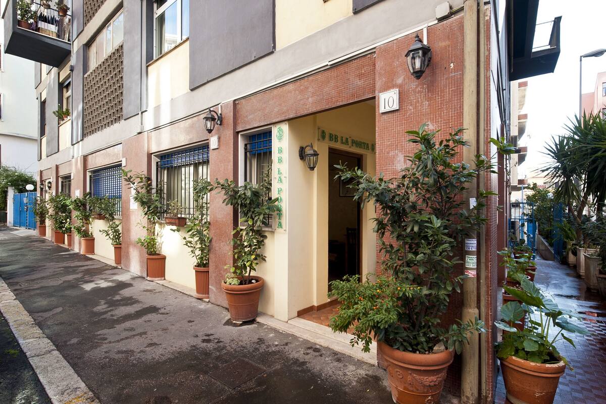A narrow street lined with potted plants and a building with a sign reading "BB LA PORTA".