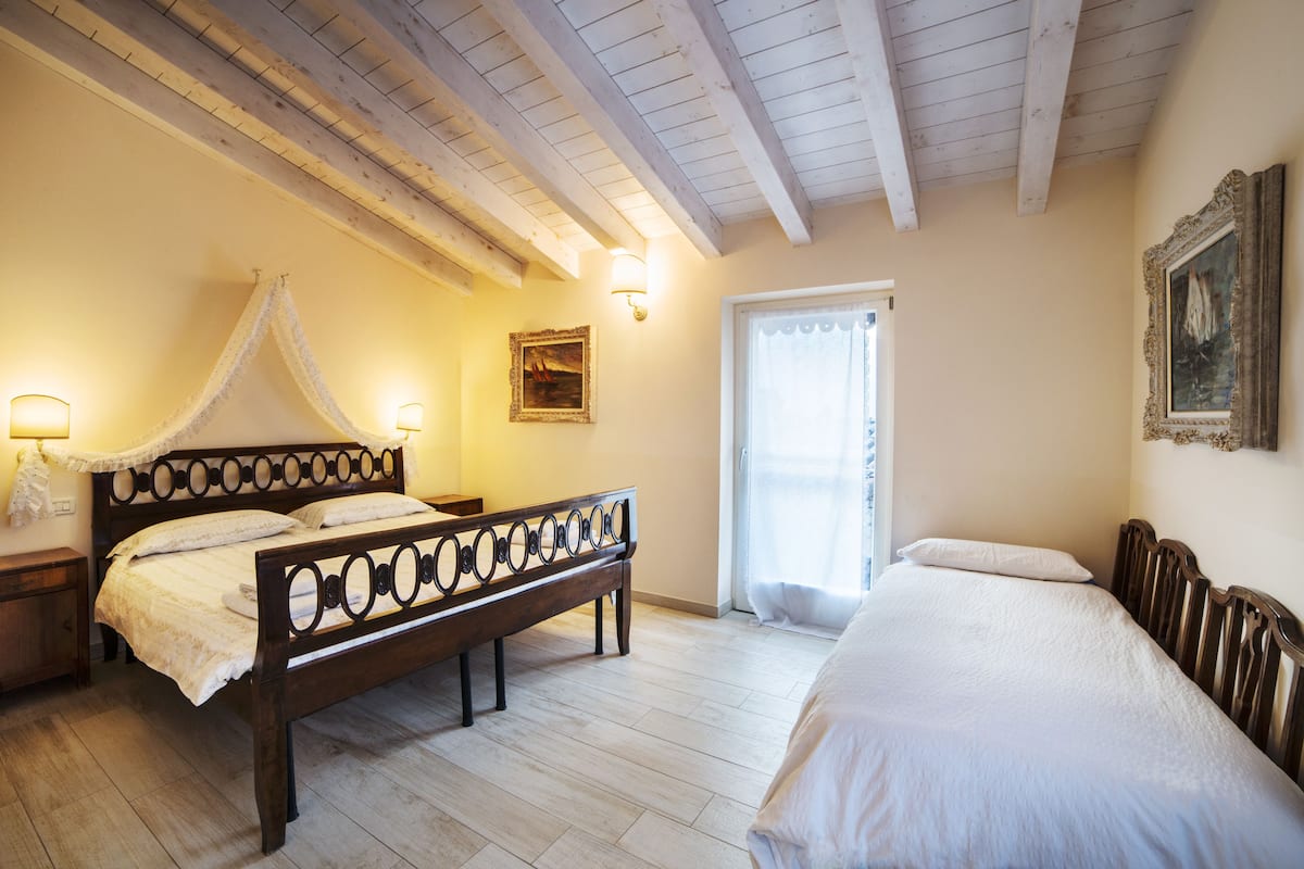 A bedroom with a four-poster bed, a nightstand, a bedside table, a window with curtains, and a painting on the wall.