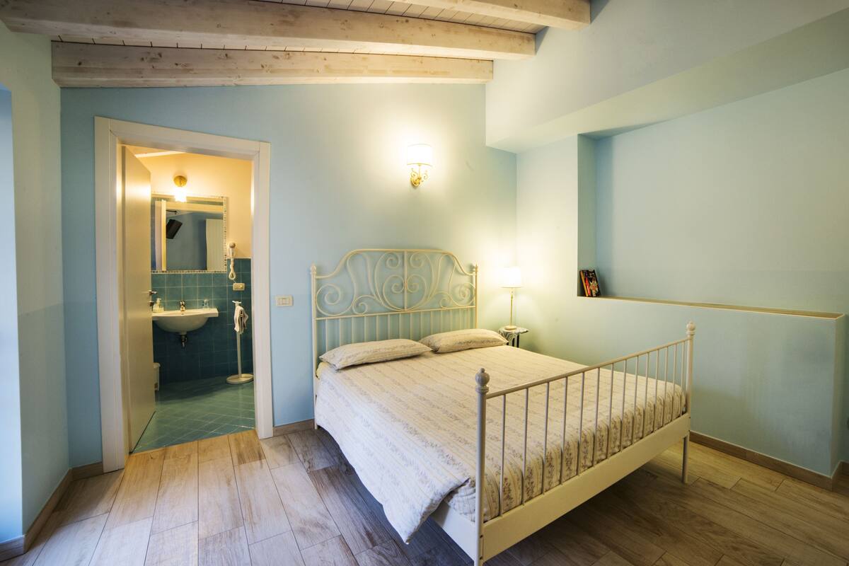 A bedroom with a bed, a nightstand, a wall-mounted lamp, and a bathroom visible through an open door.