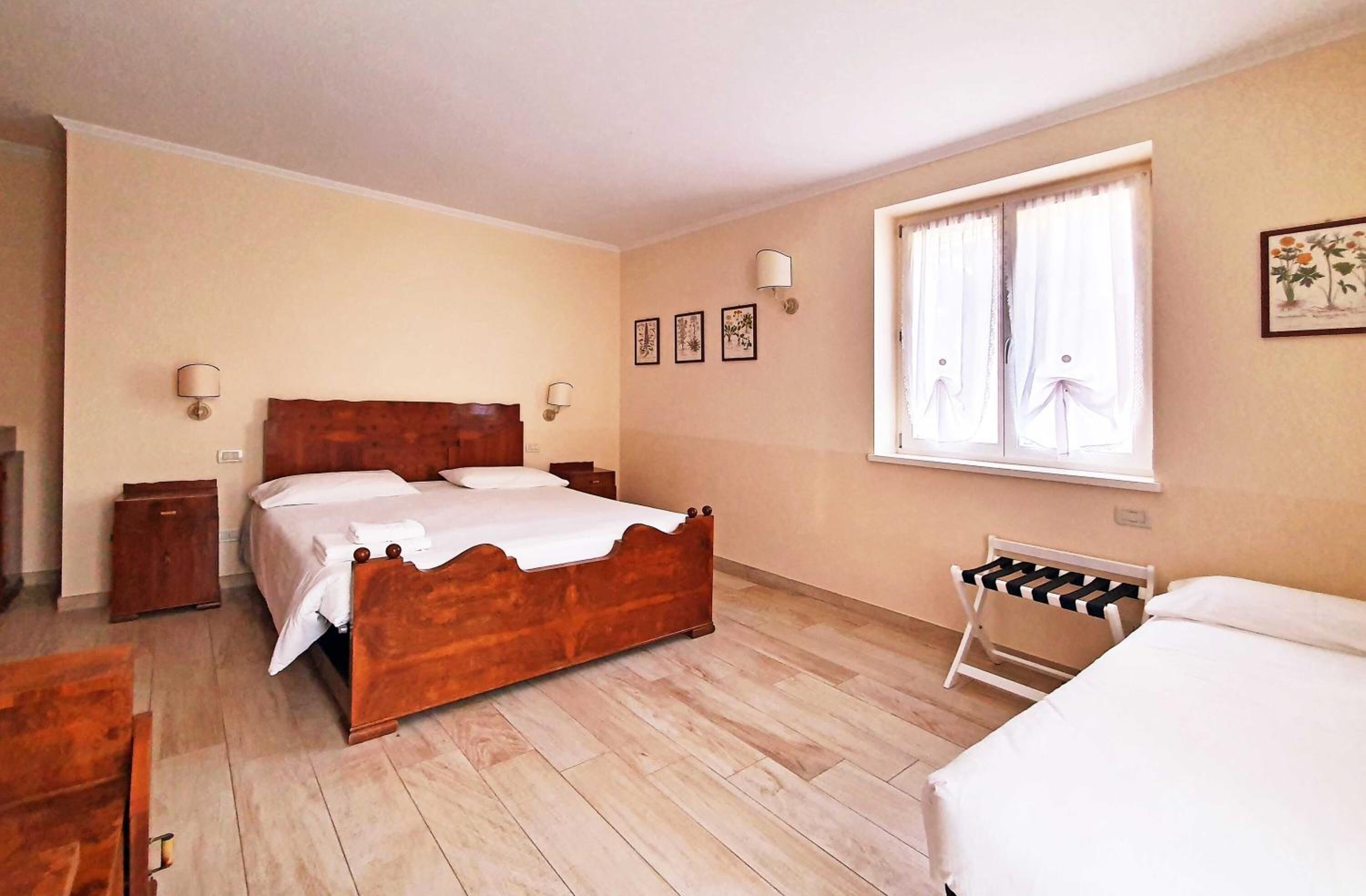 A bedroom with a wooden bed, a bedside table, a chair, a window with curtains, and wall-mounted lamps.
