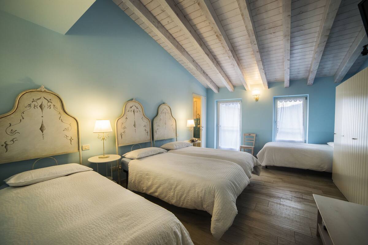 A bedroom with four beds, wooden beams on the ceiling, and a small round table with a lamp.