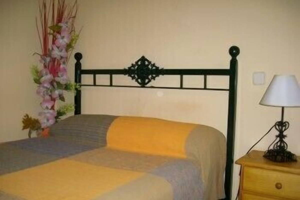 A bed with a decorative headboard, a bedside table with a lamp, and a floral arrangement.