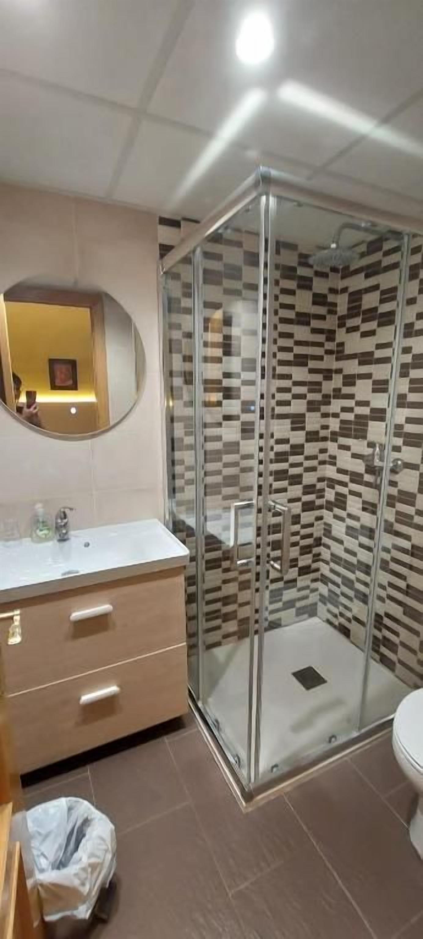 A bathroom with a glass-enclosed shower, a sink with a mirror, and a tiled wall.