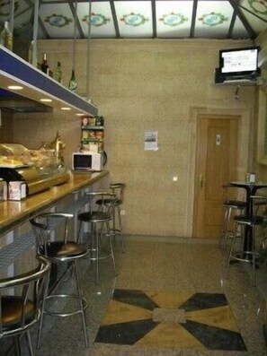 A bar area with stools, a counter, and a television screen. - Hostal DS (Velilla de San Antonio)