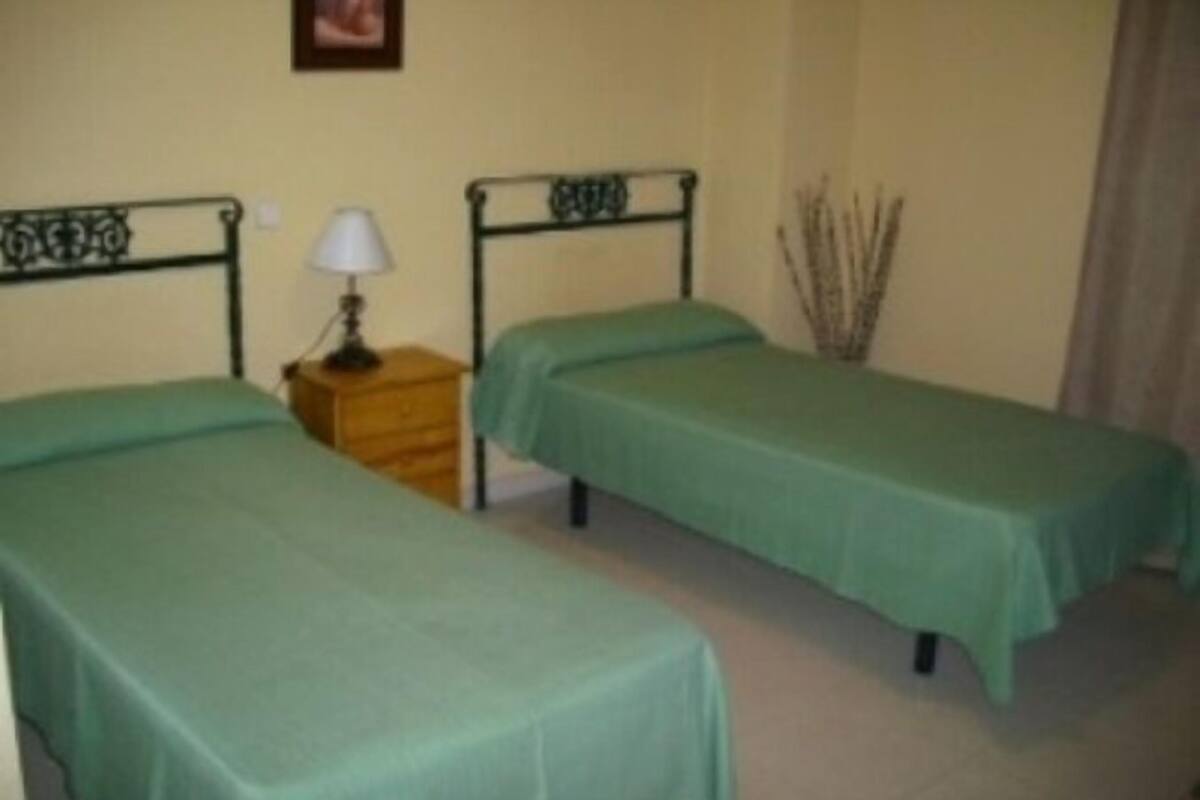 A room with two single beds, a wooden nightstand with a lamp, and a vase with branches.