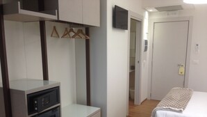 Un dormitorio con cama, armario, televisor y una pequeña kitchenette.