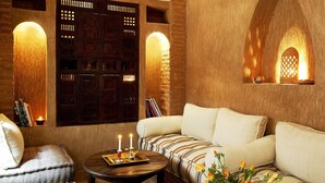 A cozy room with a cushioned sofa, a small round table with candles, and a decorative wall with wooden panels and a lantern. - Hotel Riad Carina (Marrakech)
