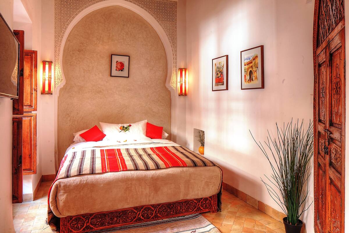 A bedroom with a large bed, a wooden door, and two wall-mounted lights.