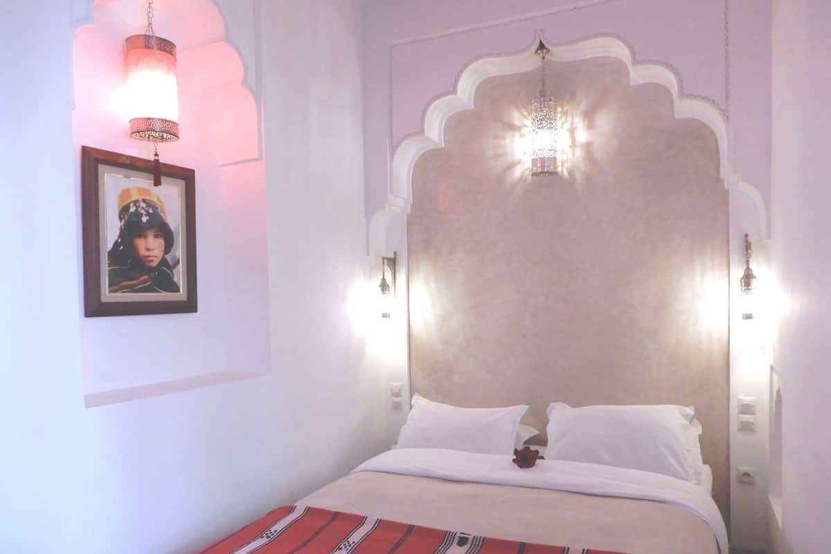 A bedroom with a bed, a framed picture on the wall, and two wall-mounted lights.