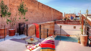 A rooftop terrace with a pool, potted plants, and a striped towel on a lounge chair. - Hotel Riad Carina (Marrakech)