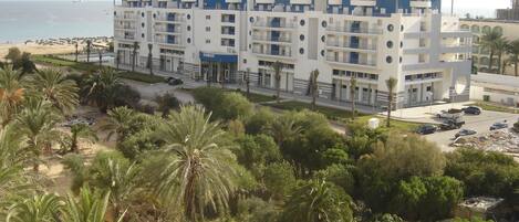 A multi-story hotel with balconies, located near a beach.
