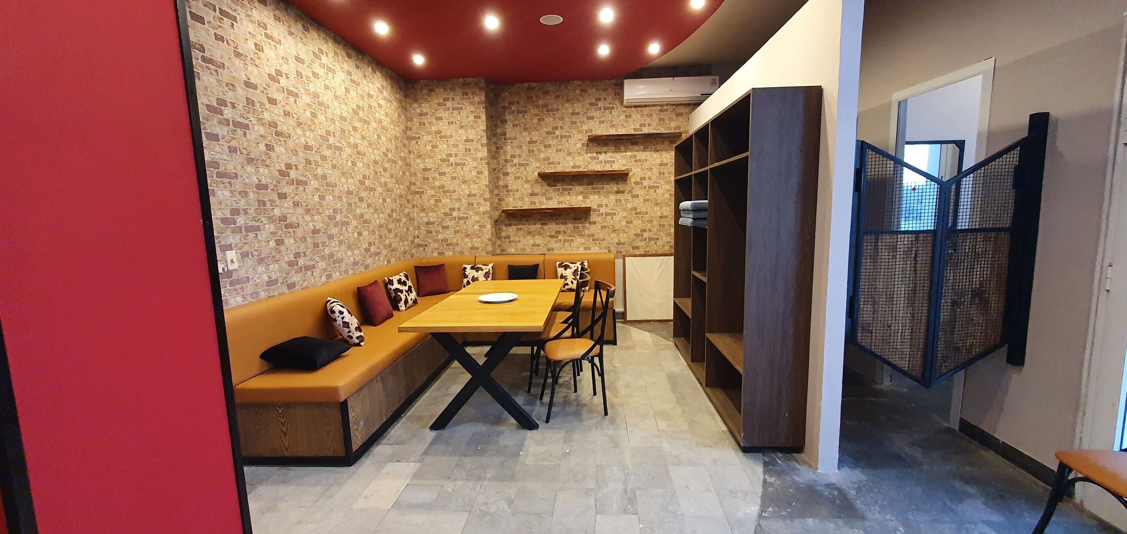 A cozy room with a brick wall, a wooden bench with cushions, a wooden table, and a bookshelf.